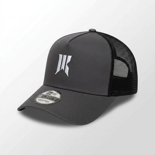 Three-quarter product shot of the charcoal Rebellion Trucker Hat with white sigil and New Era tag.