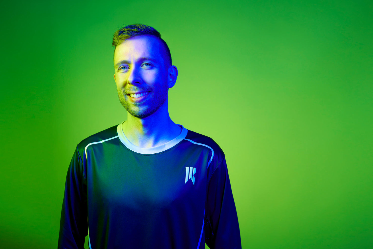 Dario smiling at the camera, wearing a black long sleeve with the Rebellion logo. Large green background behind him