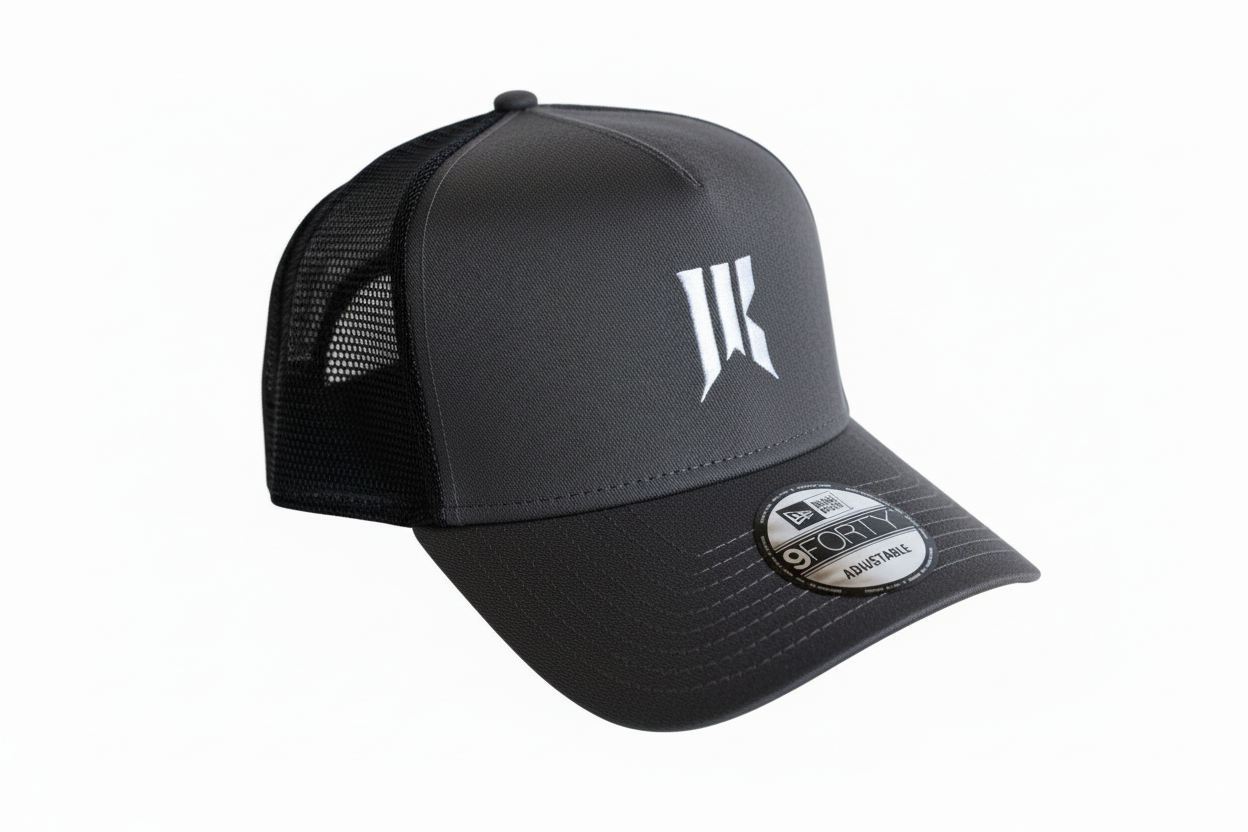 Three-quarter product shot of the charcoal Rebellion Trucker Hat with white sigil and New Era tag.
