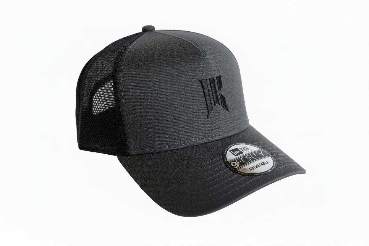 Three-quarter product shot of the charcoal Rebellion Trucker Hat with black sigil and New Era tag.